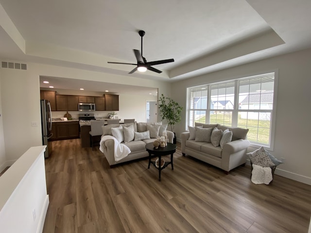 living room featuring a tray ceiling, dark wood-style floors, visible vents, and a ceiling fan