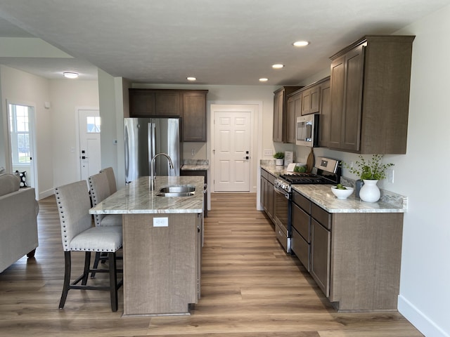 kitchen with dark brown cabinetry, a sink, a kitchen bar, stainless steel appliances, and light wood-style floors