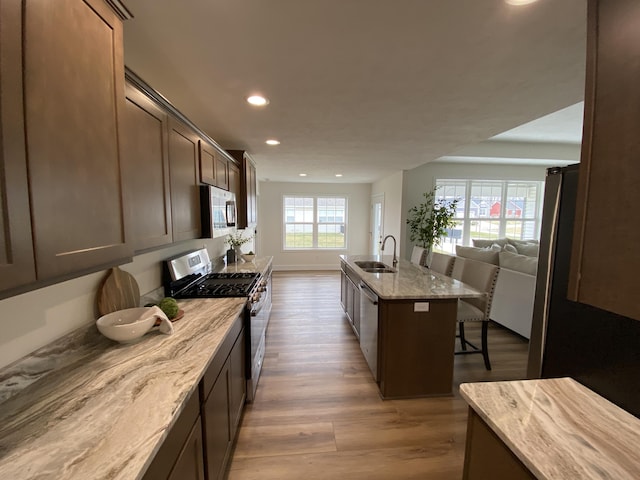 kitchen with open floor plan, a kitchen breakfast bar, a sink, light stone counters, and appliances with stainless steel finishes