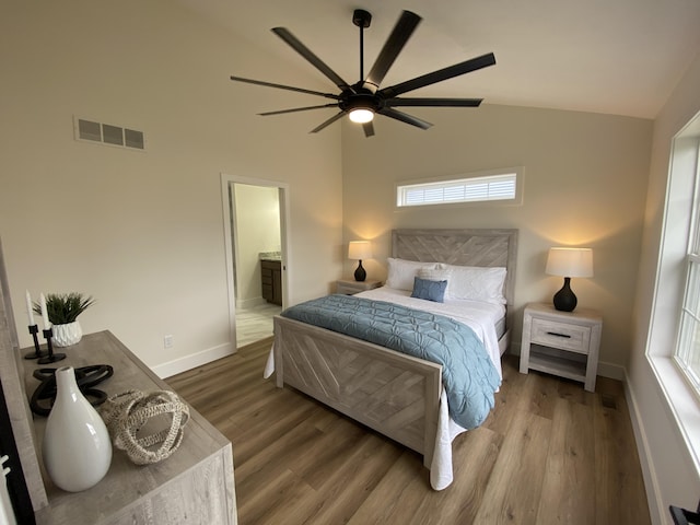 bedroom with vaulted ceiling, baseboards, ensuite bath, visible vents, and wood finished floors