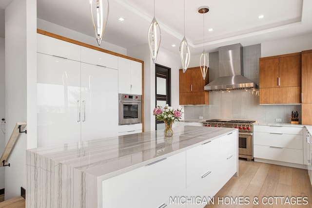 kitchen featuring wall chimney exhaust hood, light stone countertops, a large island, white cabinetry, and stainless steel appliances