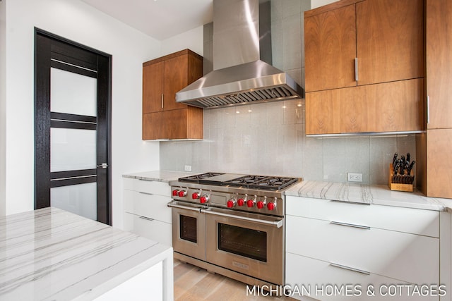 kitchen with double oven range, white cabinets, wall chimney exhaust hood, tasteful backsplash, and light stone counters