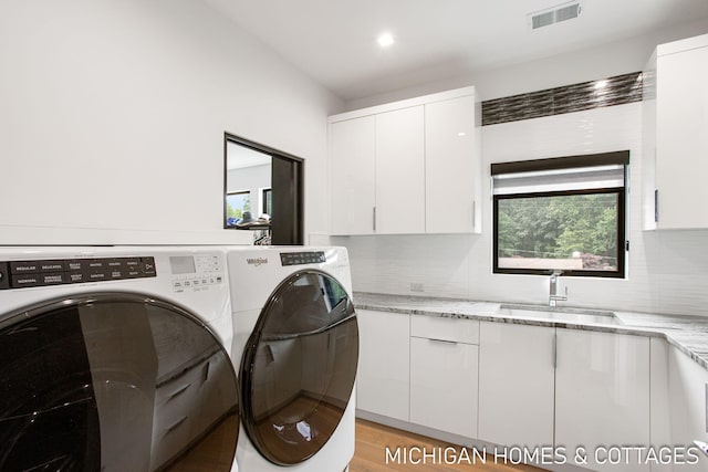 laundry area featuring washer and dryer, cabinets, sink, and light hardwood / wood-style flooring