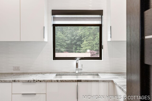 interior space with tasteful backsplash, light stone counters, sink, and white cabinets