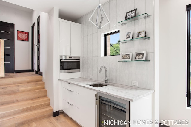 kitchen featuring sink, decorative light fixtures, light stone counters, white cabinetry, and beverage cooler