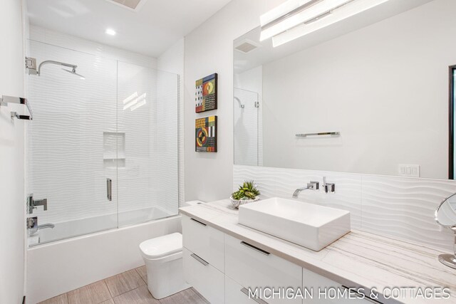 full bathroom featuring vanity, toilet, bath / shower combo with glass door, and backsplash