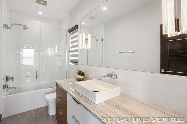 full bathroom with shower / bath combination with glass door, vanity, tile walls, and toilet