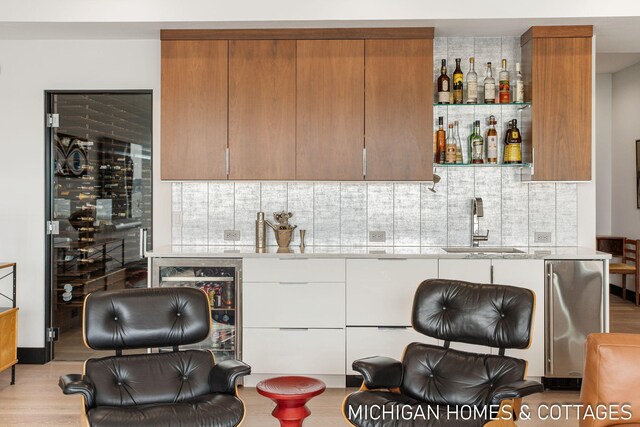 kitchen with sink, wine cooler, light hardwood / wood-style flooring, decorative backsplash, and white cabinets