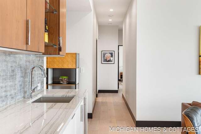 kitchen featuring light hardwood / wood-style flooring, tasteful backsplash, light stone counters, and sink