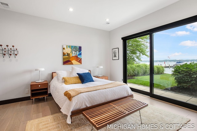 bedroom with access to exterior, a water view, and light wood-type flooring