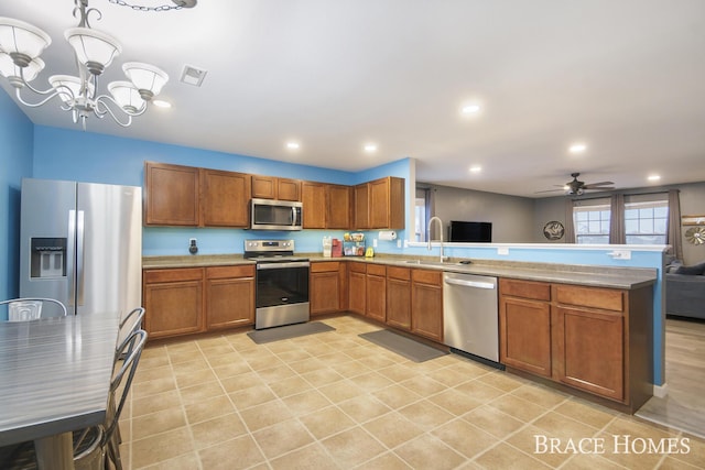 kitchen featuring kitchen peninsula, ceiling fan with notable chandelier, stainless steel appliances, sink, and pendant lighting