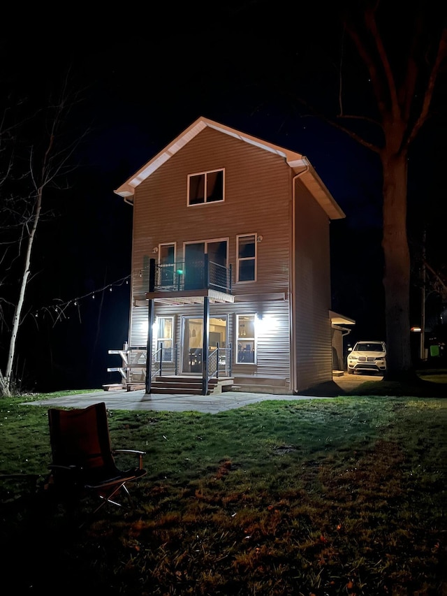 back house at night with a porch, a balcony, and a lawn