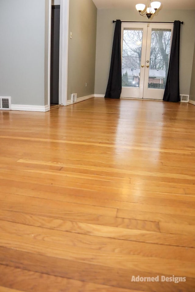 unfurnished room featuring light wood-type flooring, french doors, and a chandelier