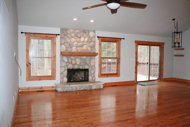 unfurnished living room featuring ceiling fan, light hardwood / wood-style floors, a stone fireplace, and a wealth of natural light