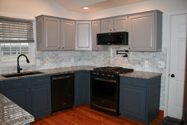 kitchen featuring dark wood-type flooring, black appliances, blue cabinets, stone counters, and sink