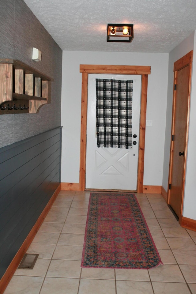 tiled entrance foyer with a textured ceiling and wood walls