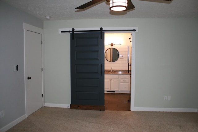 unfurnished bedroom with sink, ensuite bathroom, carpet flooring, and a barn door