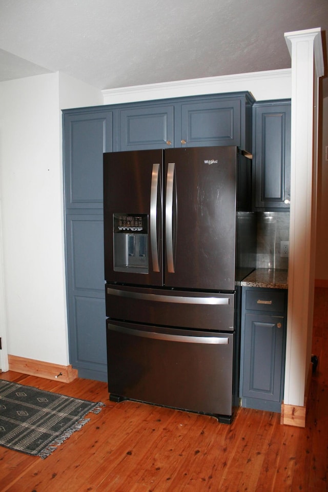 kitchen with light hardwood / wood-style floors, stainless steel fridge, dark stone countertops, and blue cabinets