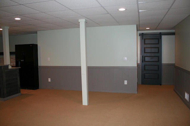 basement featuring a barn door, black refrigerator, and light carpet