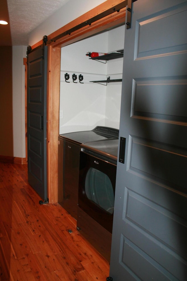 washroom featuring washing machine and dryer, wood-type flooring, a textured ceiling, and a barn door