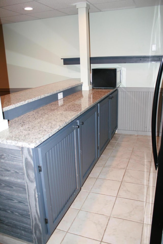 kitchen featuring blue cabinets, kitchen peninsula, a drop ceiling, and light stone countertops