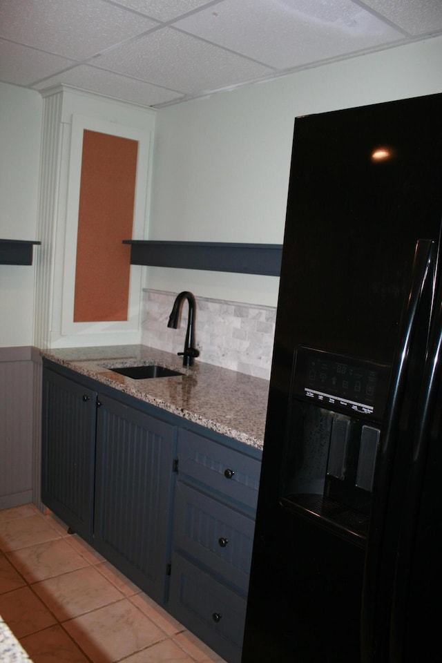 kitchen featuring black fridge, a drop ceiling, light tile patterned floors, blue cabinets, and sink