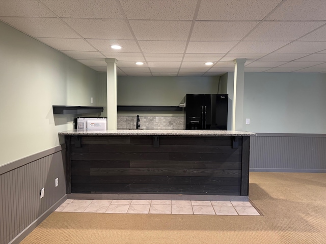 bar featuring black fridge, a paneled ceiling, and light colored carpet