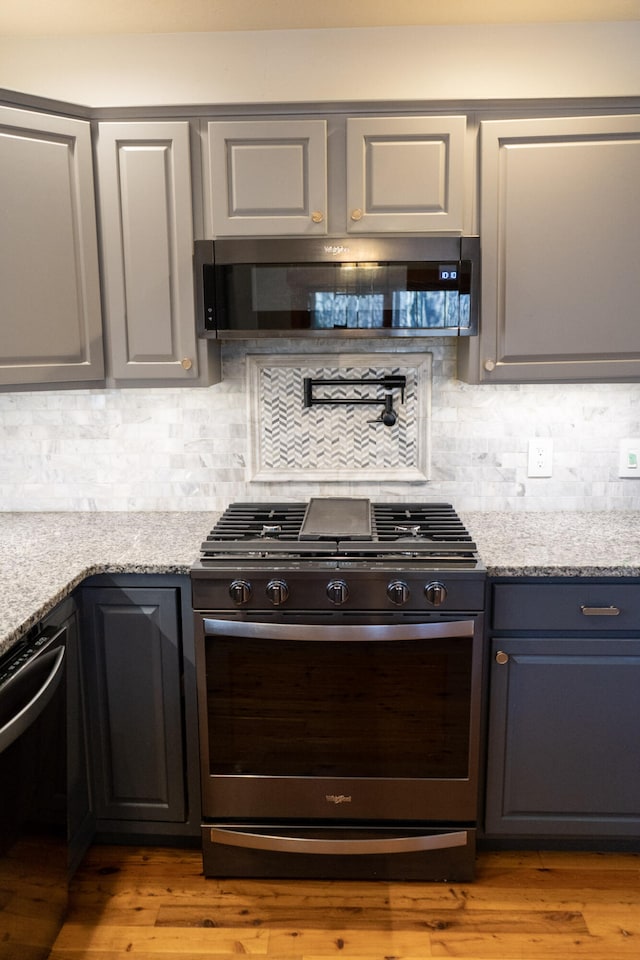 kitchen featuring stainless steel gas range, light stone counters, ventilation hood, light wood-type flooring, and dishwasher