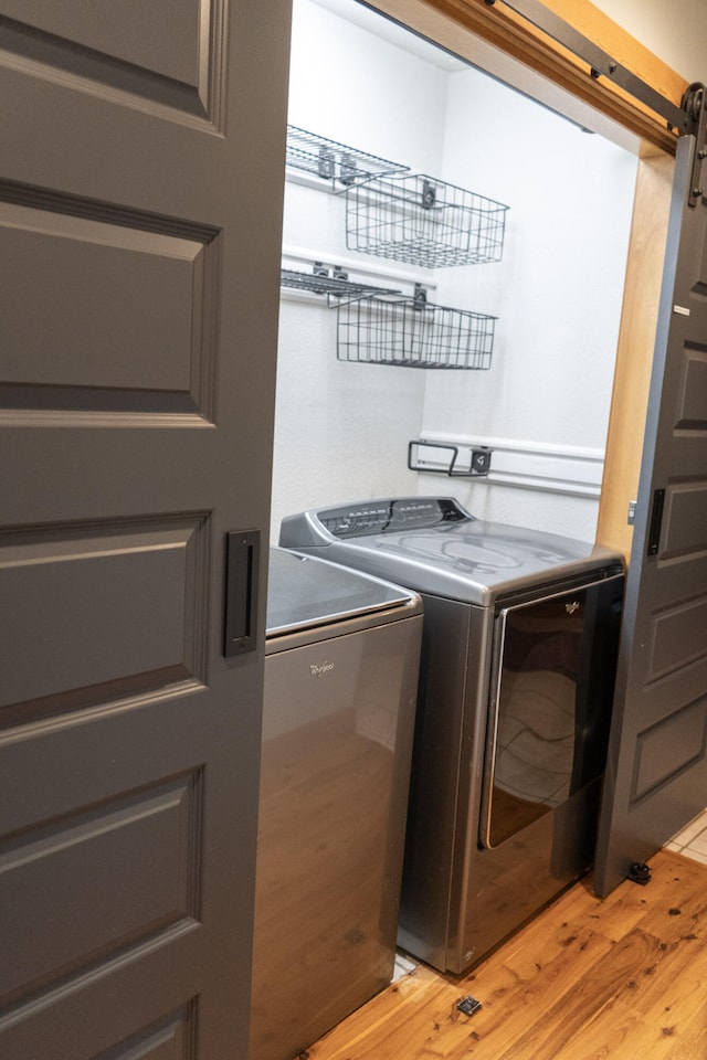 clothes washing area featuring light hardwood / wood-style floors, independent washer and dryer, and a barn door