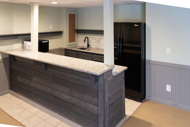 kitchen with sink, a kitchen bar, black fridge with ice dispenser, kitchen peninsula, and light stone countertops