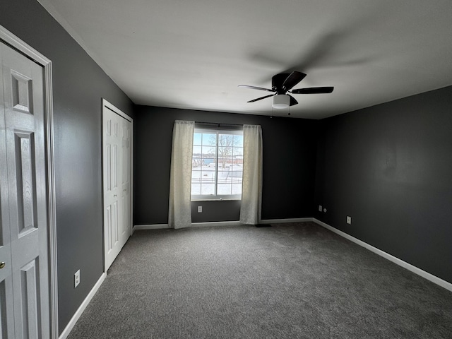 unfurnished bedroom featuring ceiling fan, dark carpet, and multiple closets