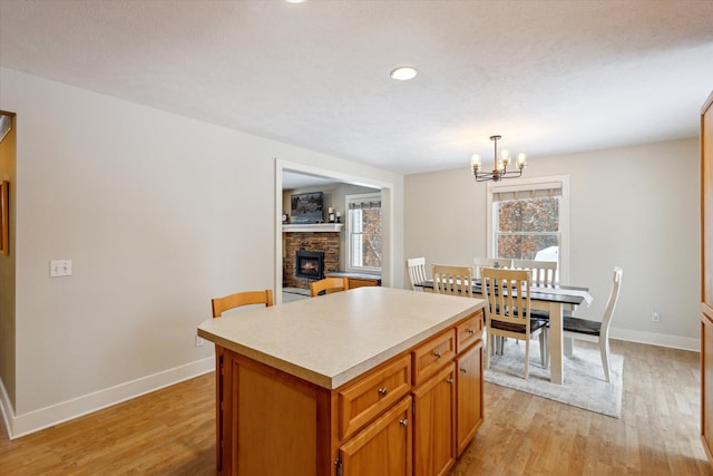 kitchen featuring an inviting chandelier, light hardwood / wood-style flooring, a fireplace, decorative light fixtures, and a kitchen island