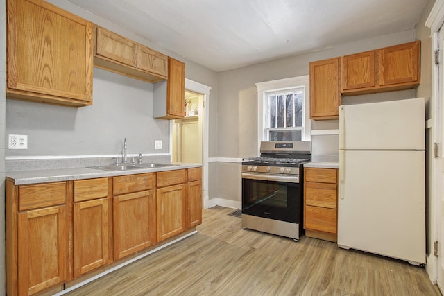 kitchen featuring stainless steel gas range oven, white fridge, sink, and light hardwood / wood-style floors