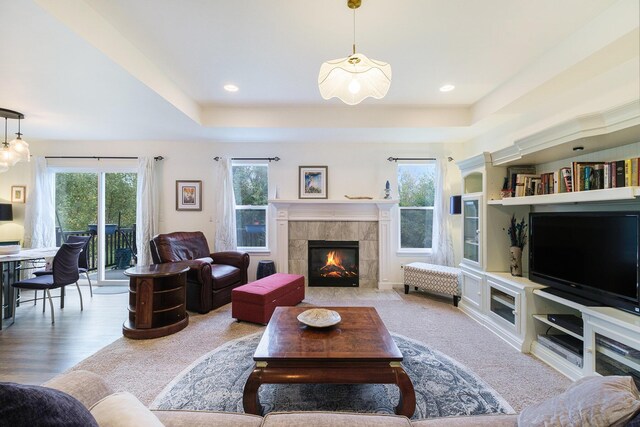 living room featuring a raised ceiling, built in features, and a tiled fireplace