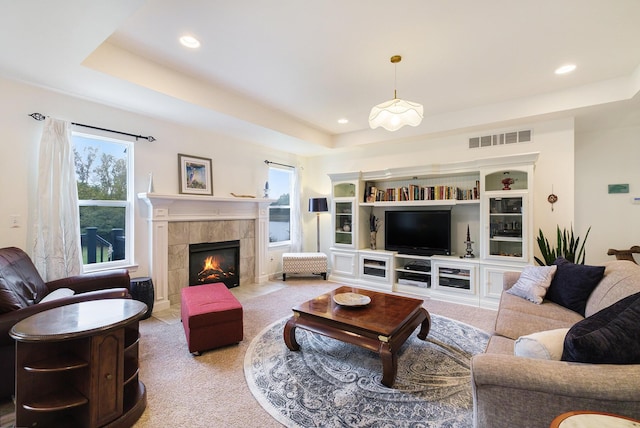 living room featuring a tiled fireplace, light carpet, and a tray ceiling