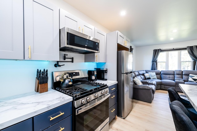 kitchen with light wood-type flooring, light stone counters, stainless steel appliances, blue cabinetry, and white cabinetry