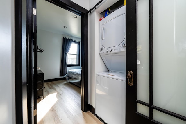 laundry room with stacked washer / drying machine and light hardwood / wood-style floors