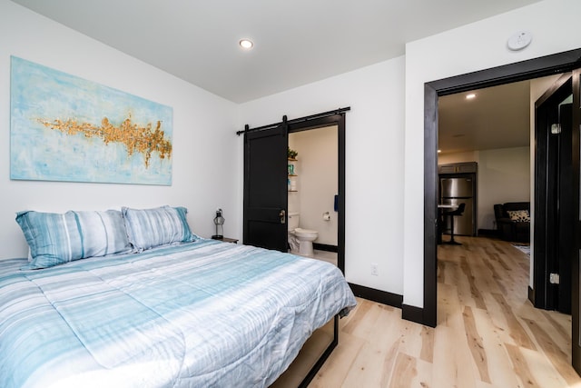 bedroom featuring stainless steel fridge, a barn door, ensuite bathroom, and light hardwood / wood-style floors