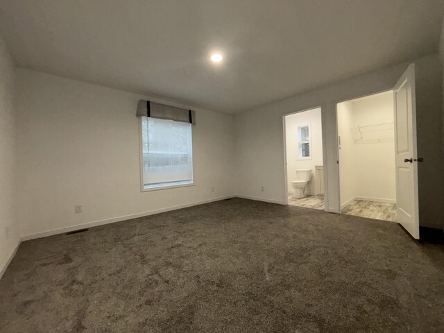 unfurnished bedroom featuring dark carpet, a spacious closet, and ensuite bath