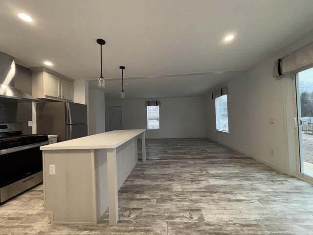 kitchen featuring wall chimney exhaust hood, appliances with stainless steel finishes, decorative light fixtures, a kitchen island, and white cabinetry