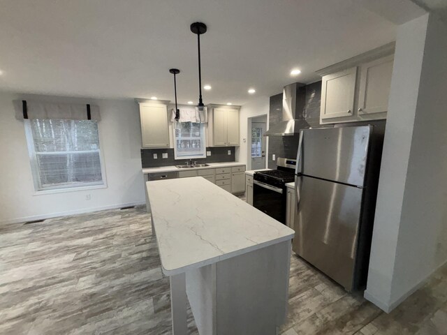 kitchen with appliances with stainless steel finishes, wall chimney exhaust hood, sink, hardwood / wood-style floors, and hanging light fixtures