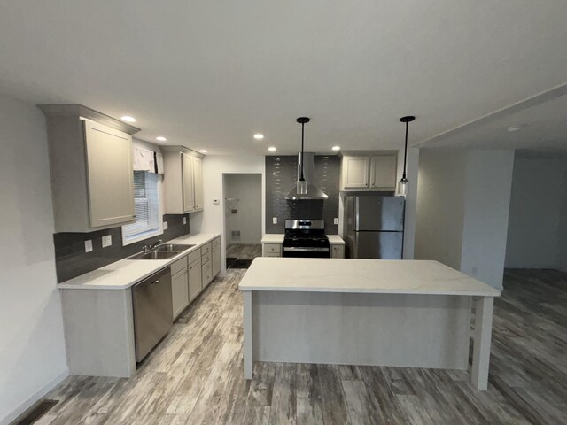 kitchen with sink, wall chimney range hood, pendant lighting, gray cabinets, and appliances with stainless steel finishes