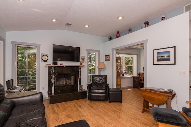 living room with a textured ceiling, light hardwood / wood-style flooring, a high end fireplace, and vaulted ceiling