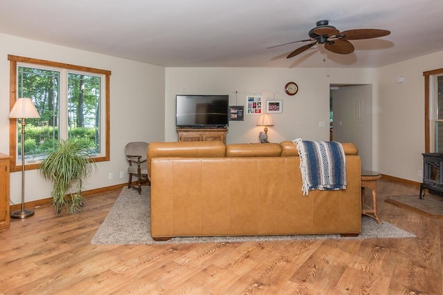 living room featuring a wood stove, ceiling fan, and light wood-type flooring