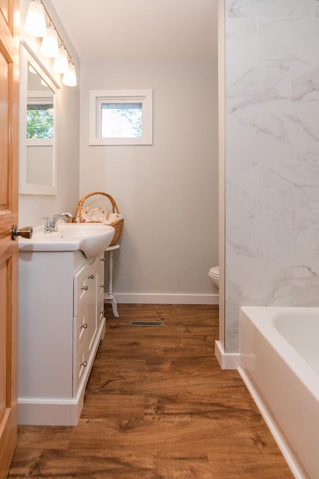 bathroom with hardwood / wood-style flooring, vanity, toilet, and a tub to relax in