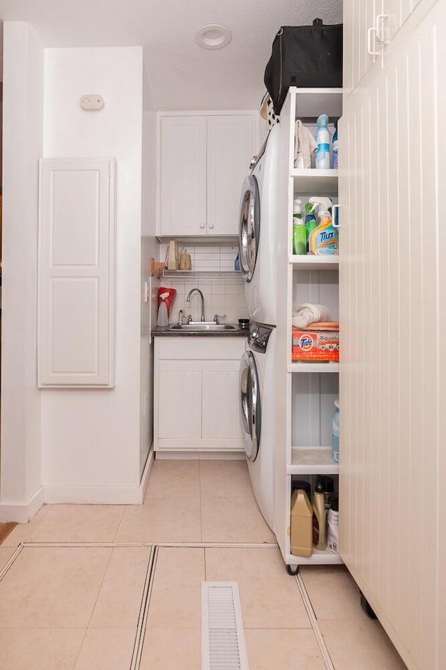 clothes washing area featuring cabinets, light tile patterned floors, stacked washing maching and dryer, and sink