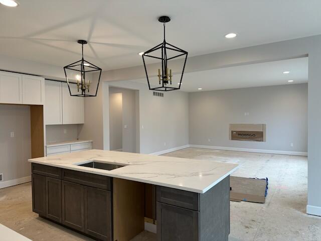 kitchen featuring baseboards, white cabinets, an island with sink, decorative light fixtures, and light stone countertops