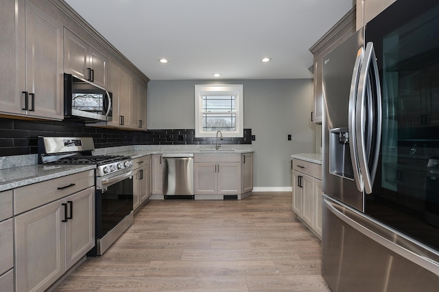 kitchen with sink, light stone counters, light hardwood / wood-style flooring, decorative backsplash, and appliances with stainless steel finishes