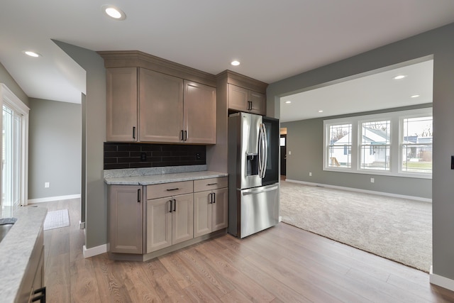 kitchen with decorative backsplash, stainless steel fridge with ice dispenser, light wood-type flooring, and light stone counters