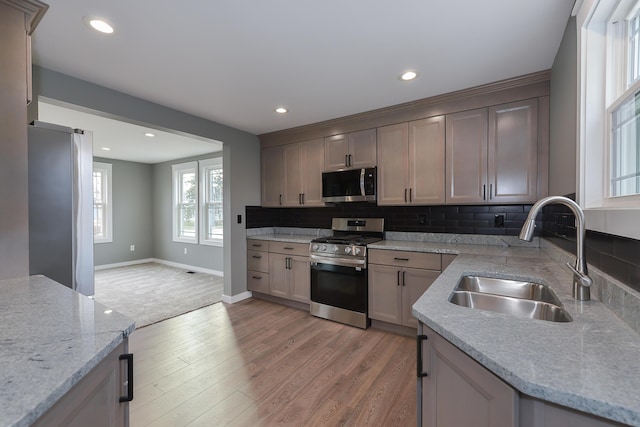 kitchen featuring sink, light stone countertops, light wood-type flooring, appliances with stainless steel finishes, and tasteful backsplash